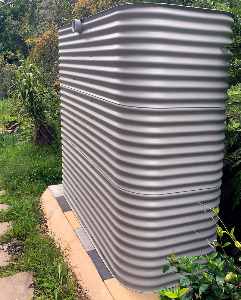 a ccwt modline water tank on a pad made form multi-coloured concrete pavers in a lush backyard